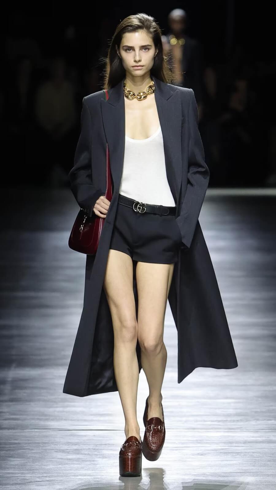 Brunette woman walking on runway with Gucci clothing and accessories.