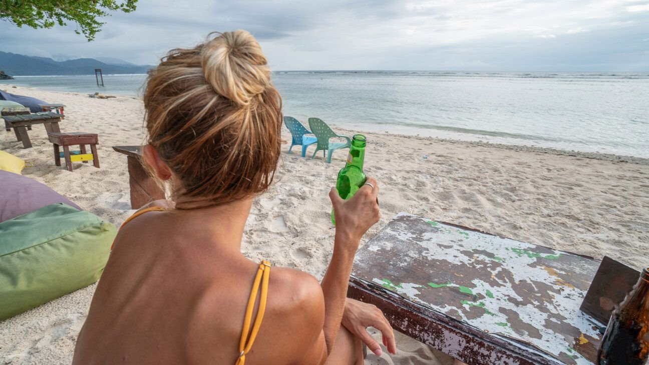 A woman on a beach holding a beer.